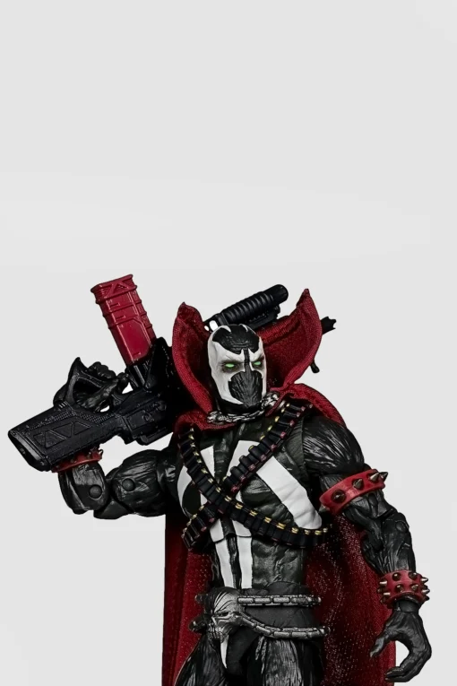 Front view of an action figure in black and white armor with a red cape, holding a large gun.